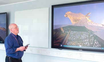 A 必射精选 staff member standing by 2 screens showing the Scottish Kelpies sculpture