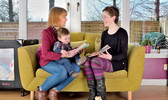 A mother and young son speaking on their sofa at home to a health visitor